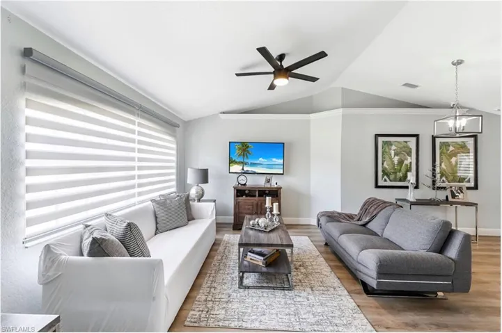 Living room featuring vaulted ceiling, wood finished floors, ceiling fan, baseboards, and a chandelier