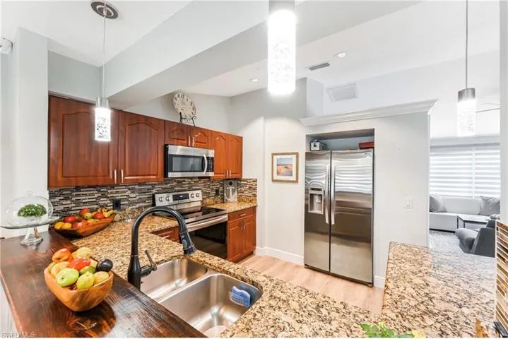 Kitchen with appliances with stainless steel finishes, a sink, decorative backsplash, light stone counters, and light wood finished floors