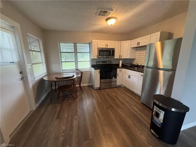 Kitchen featuring white cabinets, stainless steel appliances, dark countertops, backsplash, and a textured ceiling