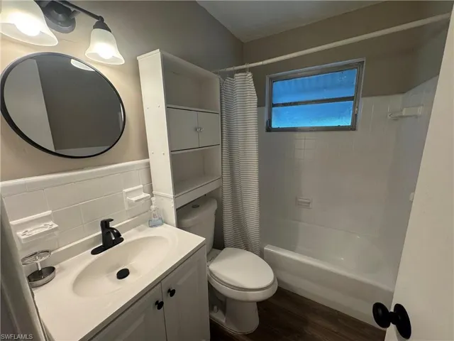 Full bathroom featuring dark wood-style floors, shower / bath combo, vanity, and tile walls