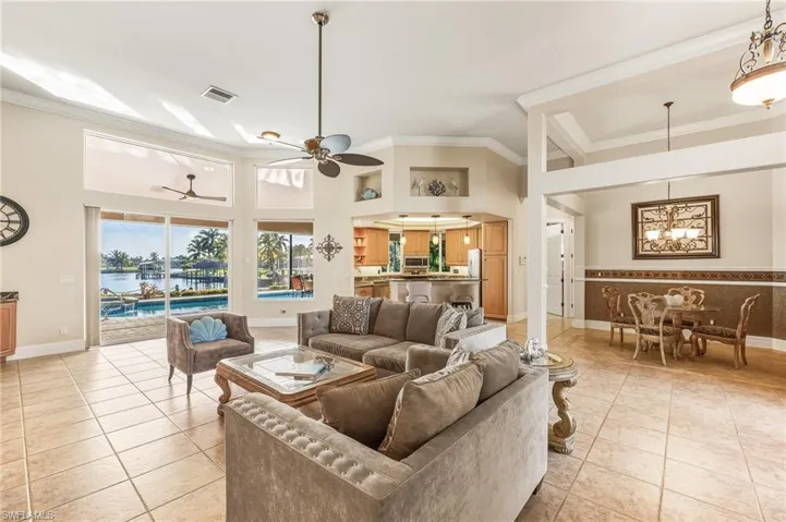 Living area with a towering ceiling, a ceiling fan, ornamental molding, a water view, and light tile patterned floors