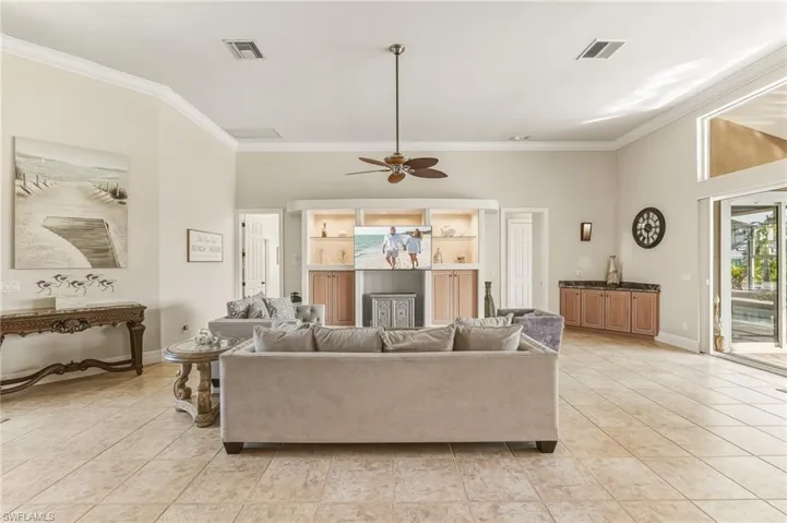 Living room with light tile patterned floors, crown molding, and a ceiling fan