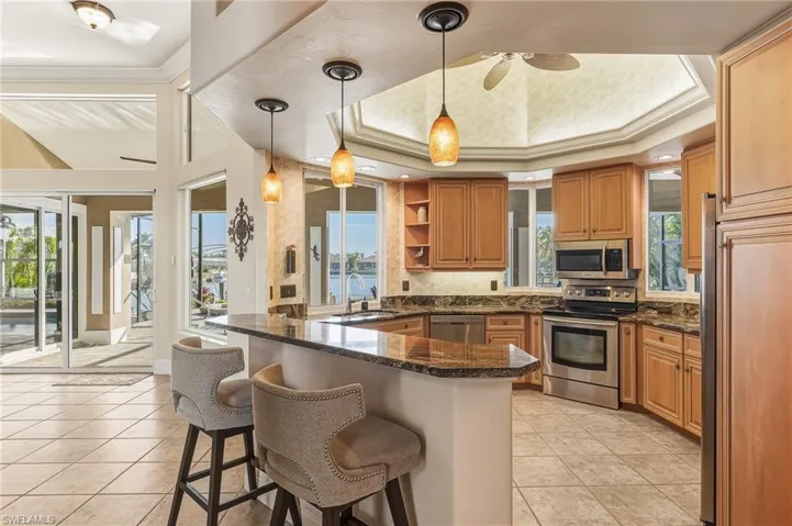 Kitchen with open shelves, appliances with stainless steel finishes, pendant lighting, dark stone counters, and ornamental molding