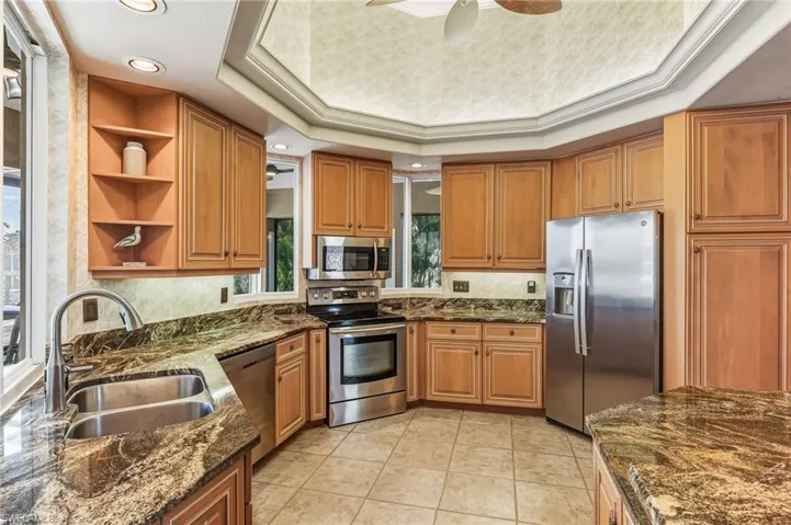 Kitchen with a raised ceiling, open shelves, stainless steel appliances, dark stone counters, and recessed lighting