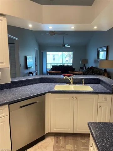 Kitchen with dishwasher, a sink, open floor plan, white cabinetry, and dark stone counters