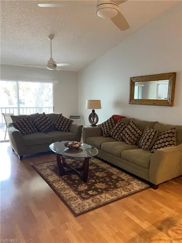 Living area featuring a ceiling fan, vaulted ceiling, wood finished floors, and a textured ceiling