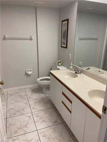 Full bath featuring double vanity, marble finish floor, a sink, and toilet