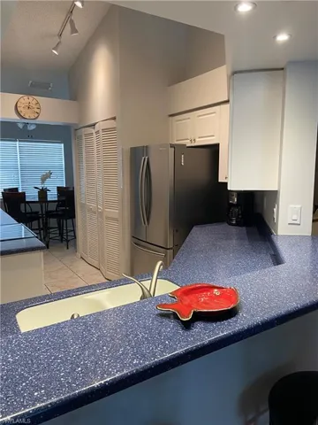 Kitchen featuring freestanding refrigerator, light tile patterned flooring, white cabinets, dark countertops, and a sink