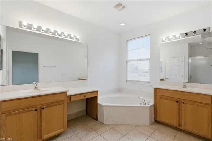 Full bathroom featuring two vanities, a stall shower, a garden tub, and light tile patterned floors