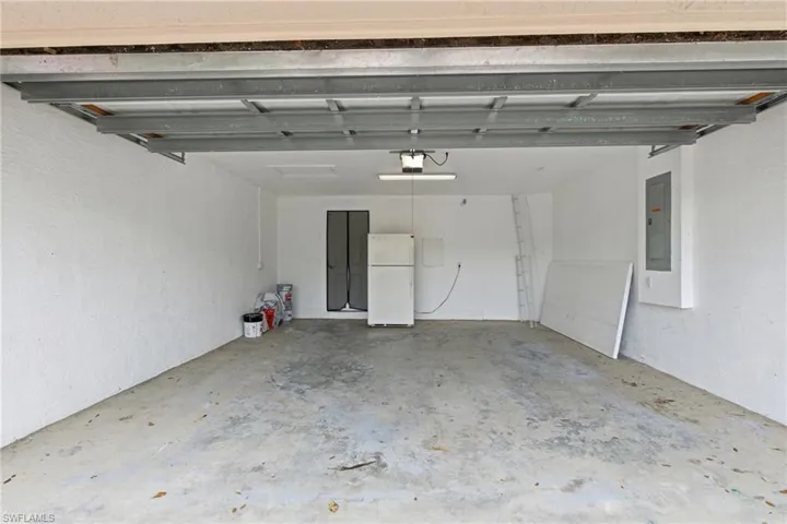 Garage featuring freestanding refrigerator, electric panel, and a textured wall