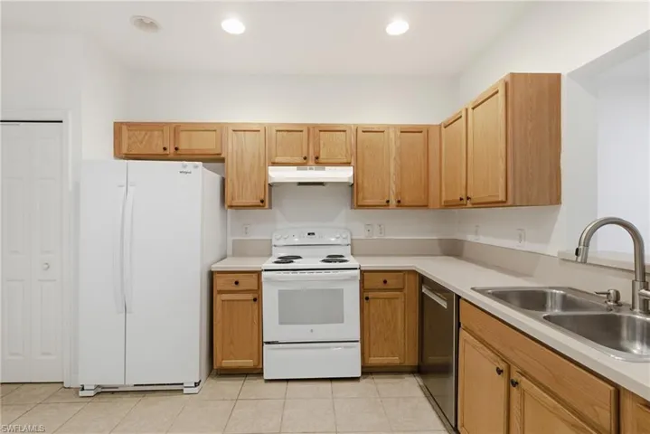 Kitchen with white appliances, light countertops, light tile patterned flooring, and recessed lighting