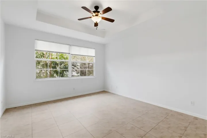 Empty room with ceiling fan, a tray ceiling, and light tile patterned flooring
