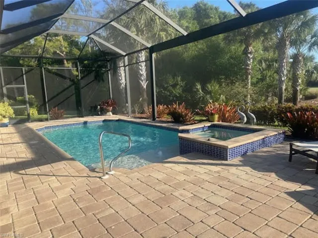 View of swimming pool with a pool with connected hot tub, a patio, and glass enclosure