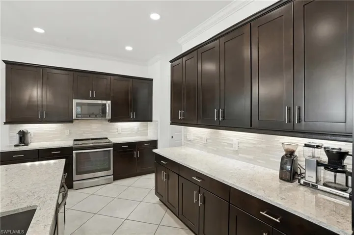 Kitchen with stainless steel appliances, decorative backsplash, light tile patterned floors, ornamental molding, and light stone counters
