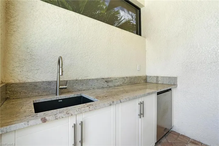 Kitchen featuring white cabinets, light stone counters, and a textured wall