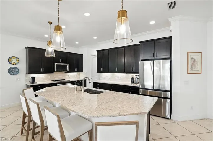 Kitchen with appliances with stainless steel finishes, dark cabinets, light tile patterned floors, decorative backsplash, and crown molding