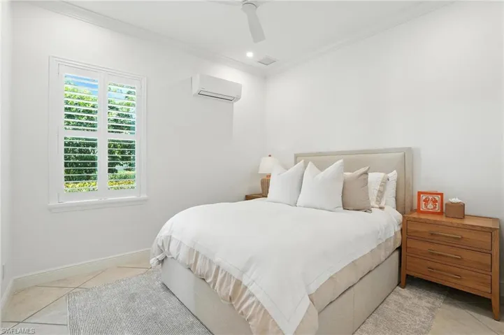 Bedroom with a wall mounted air conditioner, ornamental molding, light tile patterned floors, and ceiling fan