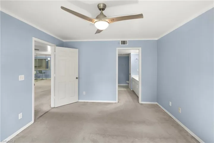 Unfurnished bedroom with carpet, a ceiling fan, ensuite bathroom, and crown molding