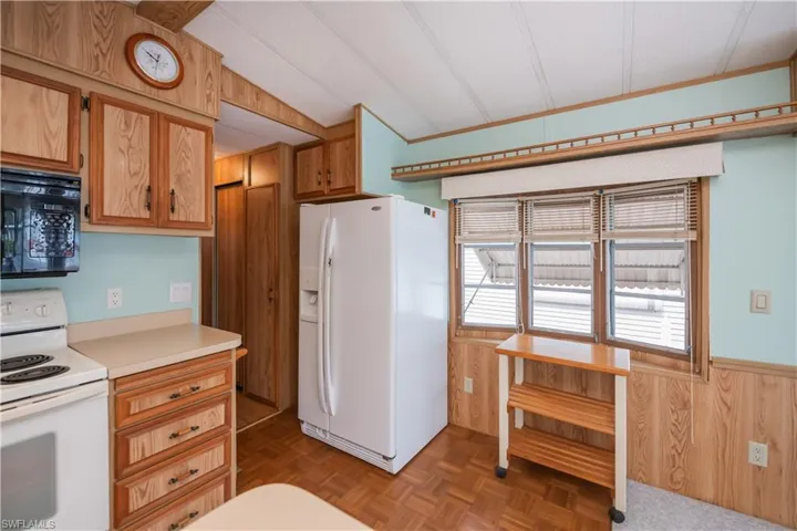 Kitchen featuring white appliances, wooden walls, wainscoting, and light countertops