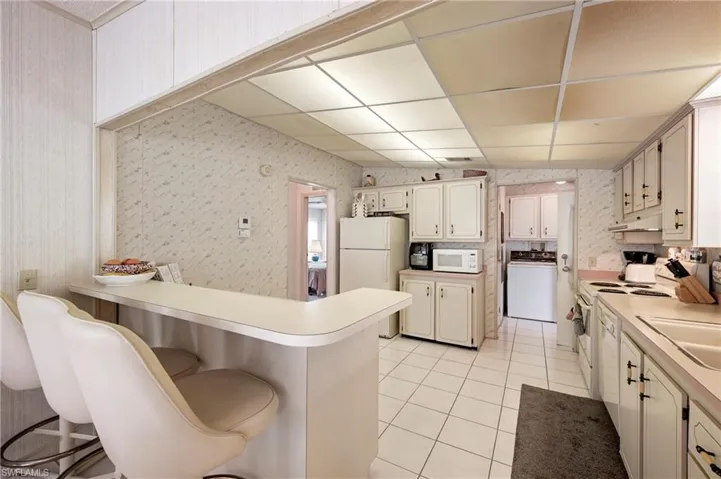 Kitchen featuring washer / dryer, white appliances, light tile patterned flooring, and wallpapered walls