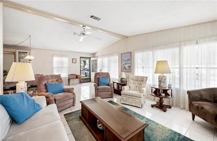 Living room with lofted ceiling with beams, a textured ceiling, a ceiling fan, visible vents, and tile patterned floors