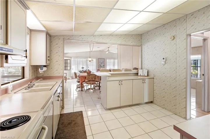 Kitchen with light tile patterned floors, a sink, light countertops, a peninsula, and wallpapered walls