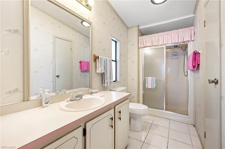 Full bathroom featuring toilet, a textured ceiling, vanity, wallpapered walls, and a stall shower