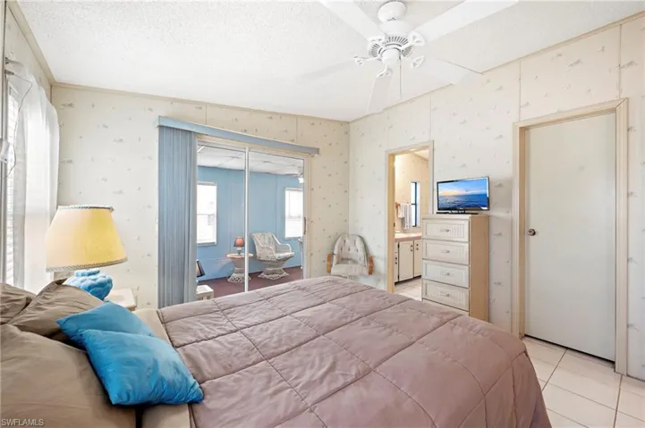 Bedroom featuring light tile patterned floors, a textured ceiling, a closet, ensuite bath, and a ceiling fan