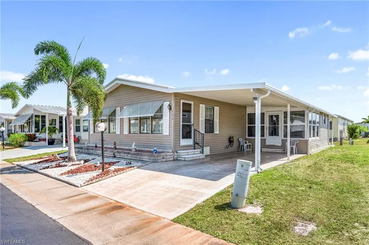 Manufactured / mobile home featuring entry steps, driveway, a front yard, and an attached carport
