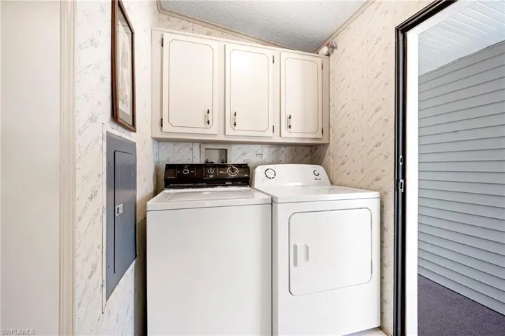 Washroom with cabinet space, a textured ceiling, washing machine and dryer, and wallpapered walls