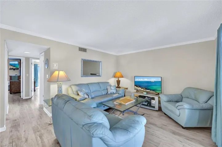 Living room with ornamental molding, light hardwood / wood-style floors, and a textured ceiling