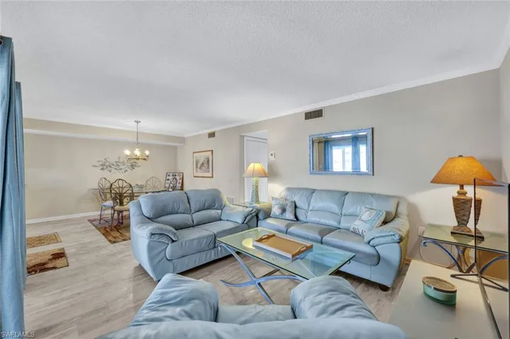 Living room featuring a notable chandelier, crown molding, a textured ceiling, and light wood-type flooring