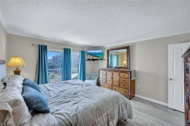 Bedroom with crown molding, access to exterior, a textured ceiling, and light wood-type flooring