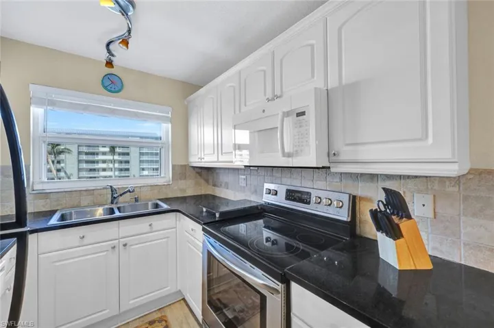 Kitchen with white cabinetry, sink, stainless steel range with electric cooktop, backsplash, and light hardwood / wood-style floors