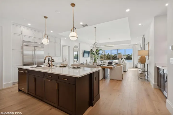 Kitchen featuring white cabinets, stainless steel built in fridge, sink, light wood-type flooring, and decorative light fixtures