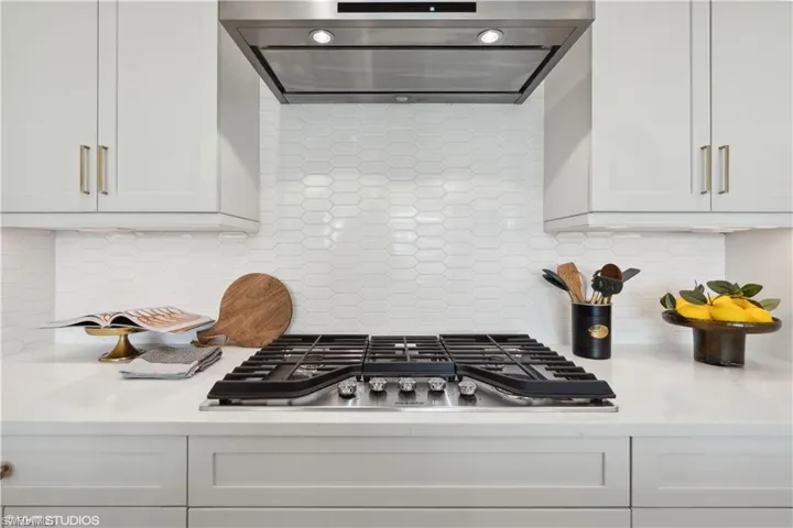 Kitchen with ventilation hood, stainless steel gas stovetop, white cabinets, and tasteful backsplash