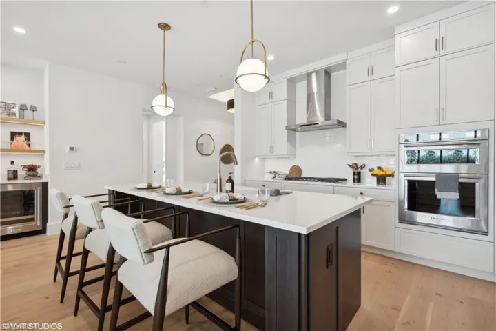 Kitchen featuring white cabinets, wall chimney exhaust hood, hanging light fixtures, and appliances with stainless steel finishes