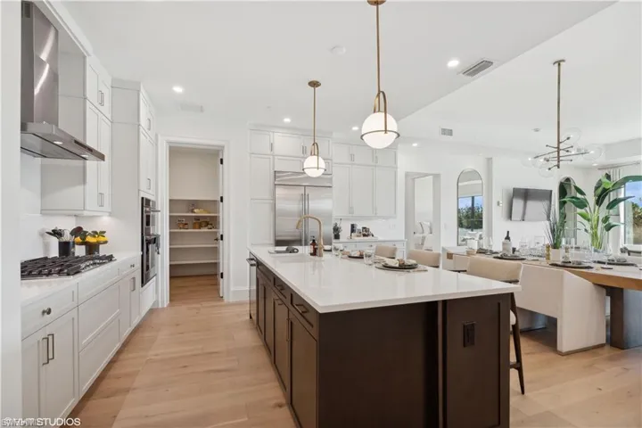 Kitchen with hanging light fixtures, wall chimney range hood, light hardwood / wood-style flooring, white cabinets, and appliances with stainless steel finishes