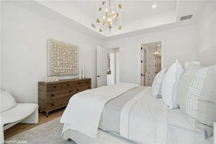 Bedroom with a raised ceiling, a notable chandelier, ensuite bath, and light hardwood / wood-style flooring