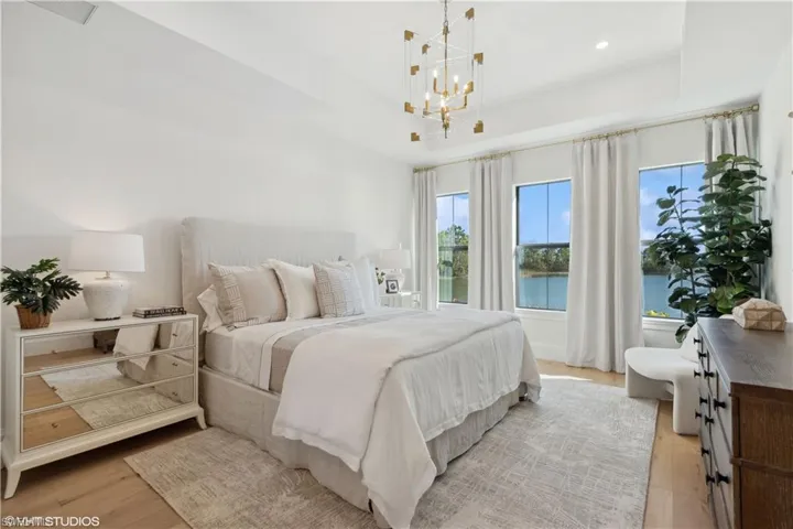 Bedroom with a notable chandelier, a water view, light wood-type flooring, and a tray ceiling