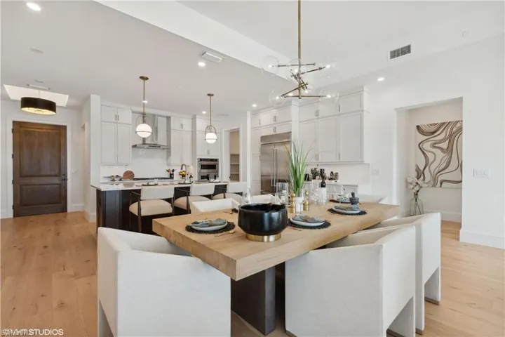 Kitchen featuring pendant lighting, wall chimney exhaust hood, light hardwood / wood-style floors, white cabinetry, and stainless steel appliances