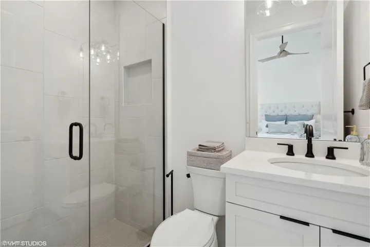 Bathroom with an enclosed shower, vanity, ceiling fan, and toilet