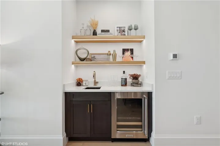 Bar featuring light tile patterned floors, dark brown cabinetry, beverage cooler, and sink