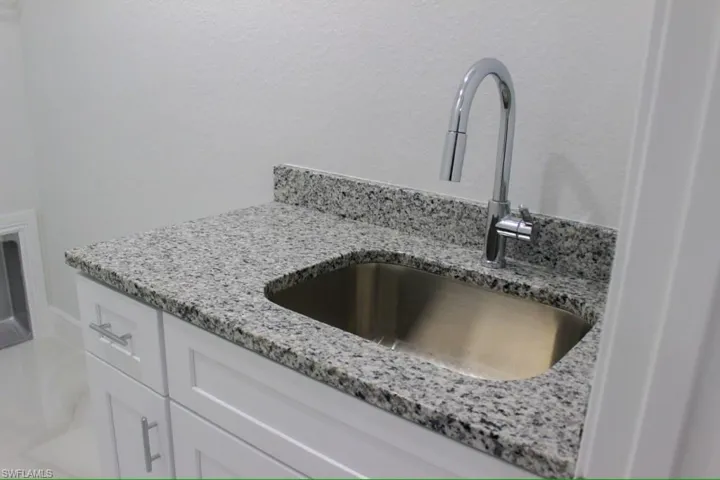 Interior details with white cabinetry, light stone counters, and a sink