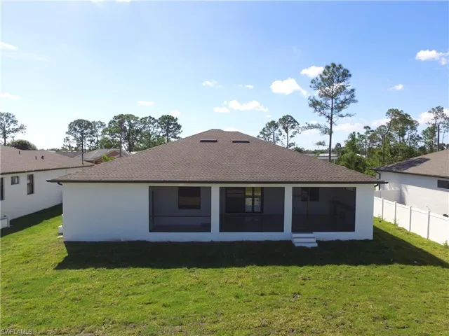 Back of house with roof with shingles, stucco siding, fence, a sunroom, and a lawn