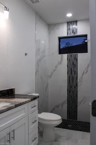 Bathroom featuring visible vents, marble finish floor, a marble finish shower, toilet, and vanity