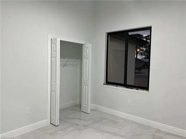 Unfurnished bedroom featuring marble finish floor, a closet, and baseboards