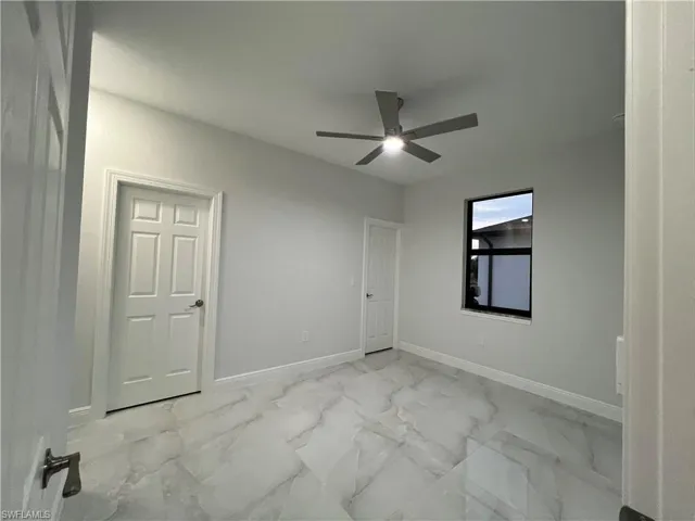 Spare room featuring marble finish floor, baseboards, and a ceiling fan