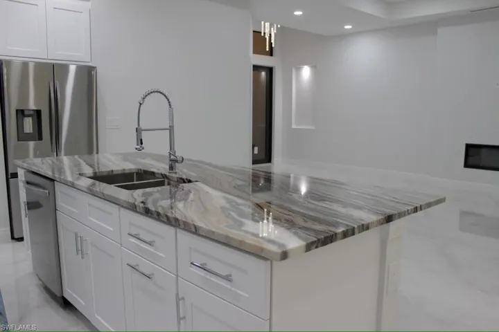 Kitchen with appliances with stainless steel finishes, white cabinetry, a spacious island, and a sink
