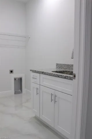 Washroom featuring hookup for an electric dryer, baseboards, marble finish floor, a sink, and cabinet space